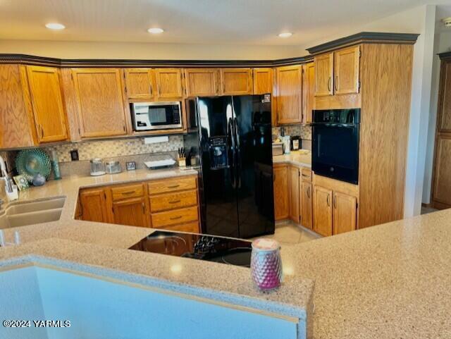 kitchen with brown cabinetry, a sink, a peninsula, and black appliances