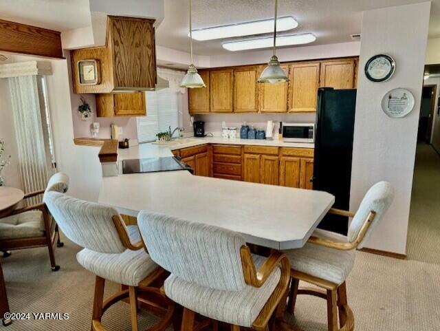 kitchen with light colored carpet, decorative light fixtures, a peninsula, light countertops, and black appliances