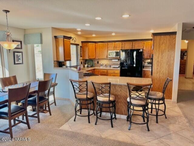 kitchen featuring stainless steel microwave, brown cabinets, freestanding refrigerator, hanging light fixtures, and a peninsula