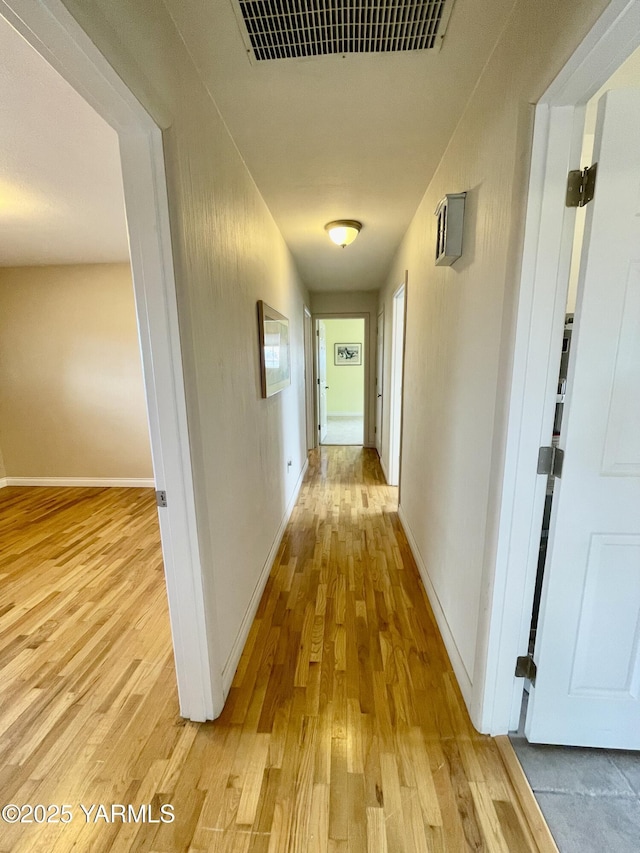 hallway with light wood-style floors, baseboards, and visible vents