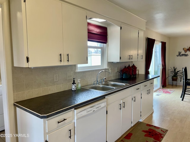 kitchen with light wood finished floors, dishwasher, dark countertops, backsplash, and a sink