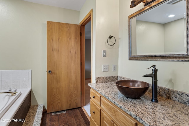 full bathroom with visible vents, wood finished floors, a bath, and vanity