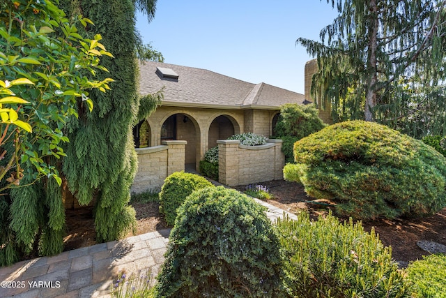 view of front of property featuring a shingled roof, a chimney, and stone siding