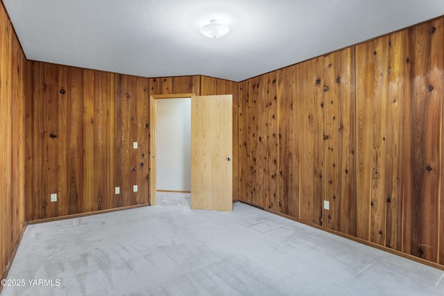 carpeted empty room with baseboards and wood walls