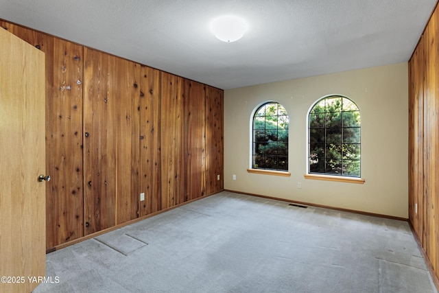 empty room featuring wooden walls, baseboards, carpet, and visible vents