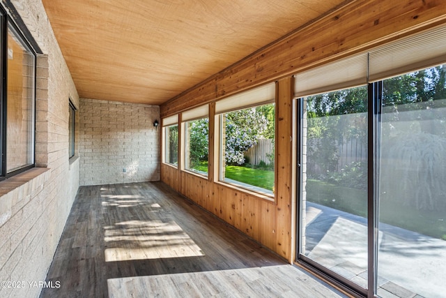 unfurnished sunroom featuring wooden walls, wooden ceiling, brick wall, and wood finished floors