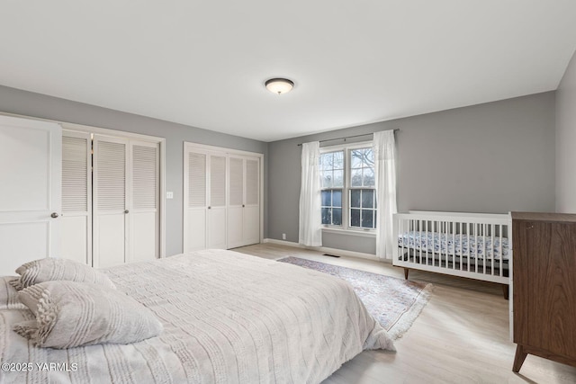 bedroom featuring visible vents, baseboards, multiple closets, and wood finished floors