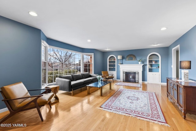 living room with built in features, light wood-style flooring, a premium fireplace, and recessed lighting