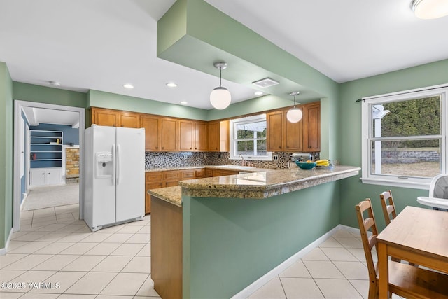 kitchen featuring a peninsula, hanging light fixtures, brown cabinets, white refrigerator with ice dispenser, and light tile patterned flooring