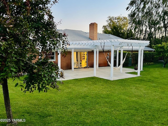 rear view of house with a patio, a chimney, a pergola, a lawn, and brick siding