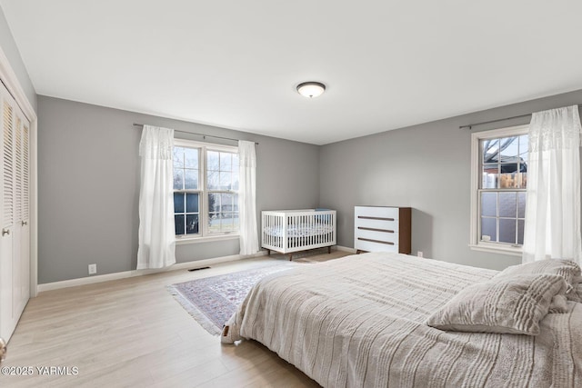 bedroom with a closet, visible vents, wood finished floors, and baseboards