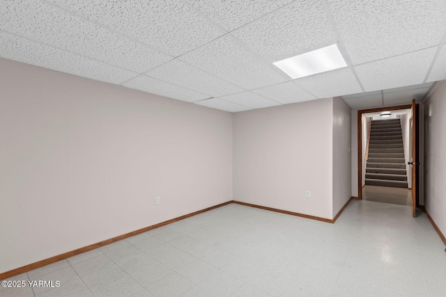 finished below grade area featuring baseboards, stairs, a drop ceiling, and light floors