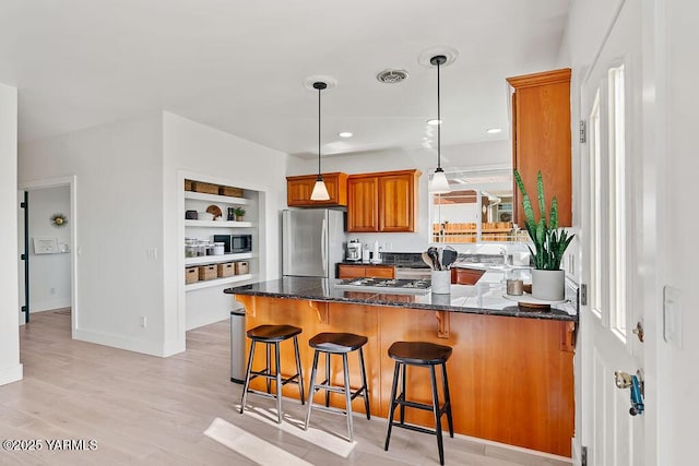 703 S 87th Ave, Yakima, WA 98908 - kitchen with freestanding refrigerator, brown cabinets, a peninsula, built in microwave, and dark stone countertops