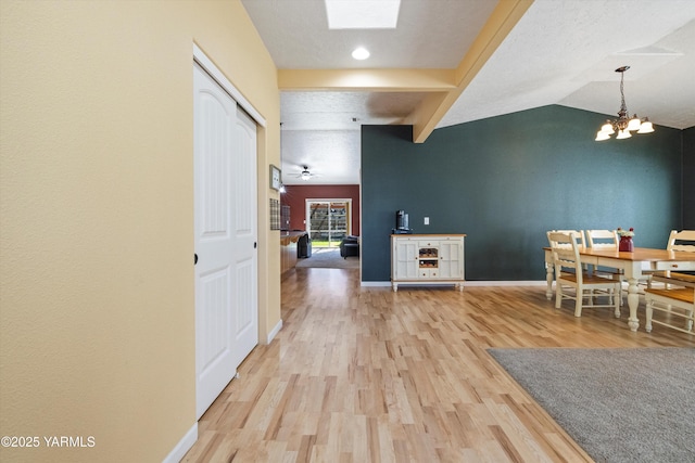 interior space with vaulted ceiling with skylight, an inviting chandelier, baseboards, and wood finished floors