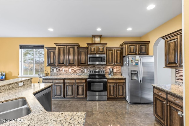 kitchen featuring arched walkways, stainless steel appliances, dark brown cabinetry, and decorative backsplash