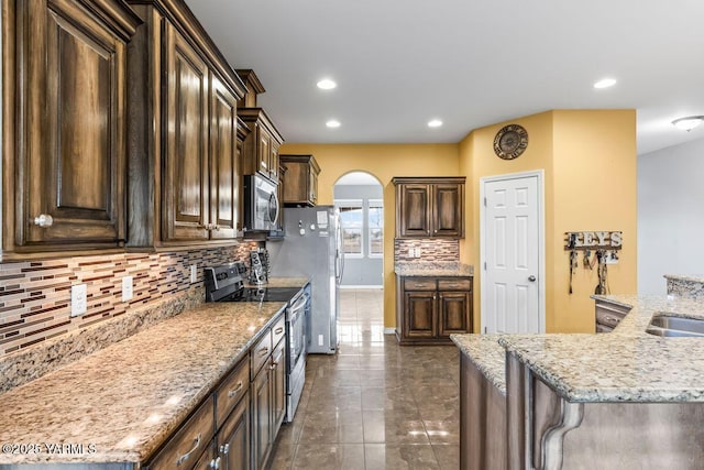 kitchen featuring arched walkways, recessed lighting, stainless steel appliances, dark brown cabinets, and tasteful backsplash