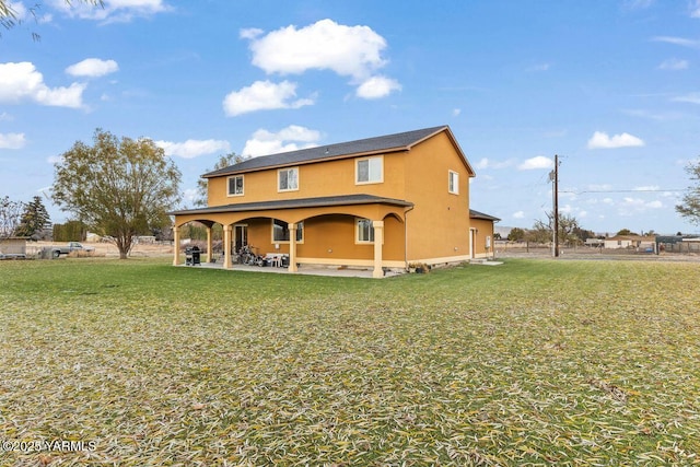 back of house featuring a patio, a lawn, and stucco siding