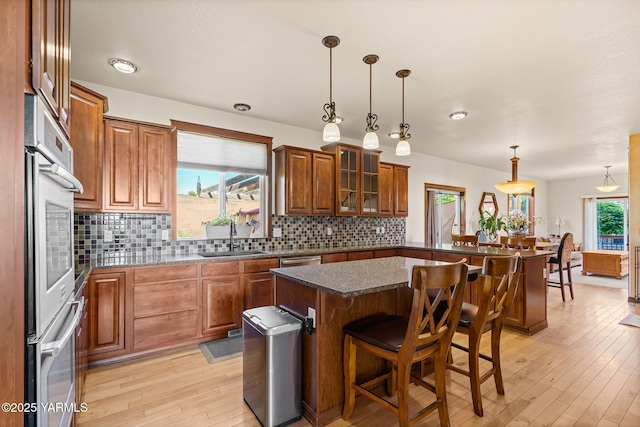 12900 Douglas Rd, Yakima, WA 98908 - kitchen featuring a sink, brown cabinetry, a breakfast bar, light wood-style flooring, and decorative backsplash