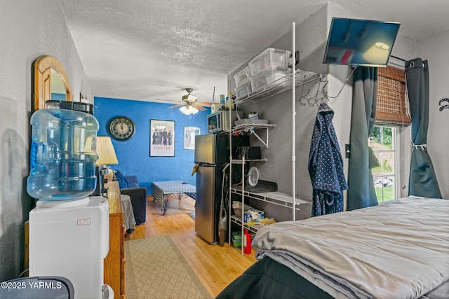 12900 Douglas Rd, Yakima, WA 98908 - bedroom featuring wood finished floors, a textured ceiling, a textured wall, freestanding refrigerator, and ceiling fan