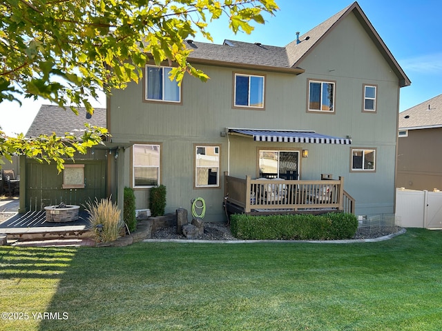 rear view of house featuring a fire pit, a shingled roof, fence, a lawn, and a wooden deck