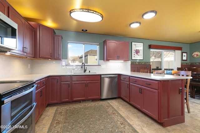 kitchen with light countertops, appliances with stainless steel finishes, a sink, a peninsula, and a kitchen bar