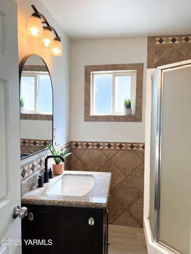 409 Elm Ave, Grandview, WA 98930 - bathroom with tile walls, a stall shower, vanity, and a wainscoted wall