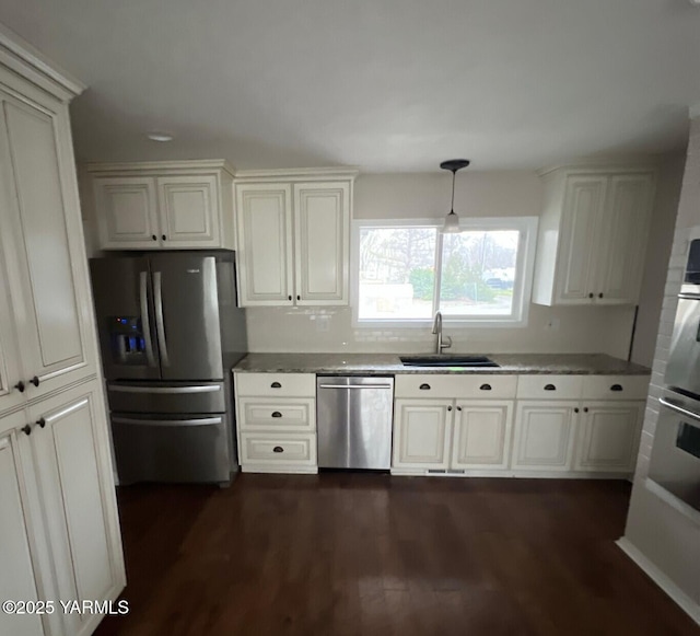 kitchen with dark wood finished floors, dark stone countertops, decorative light fixtures, stainless steel appliances, and a sink