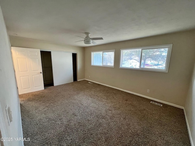 unfurnished bedroom with dark colored carpet, a closet, visible vents, a ceiling fan, and baseboards