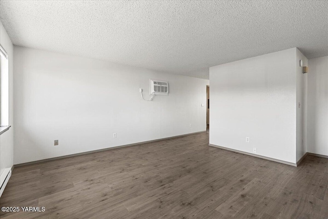 spare room featuring an AC wall unit, wood finished floors, baseboards, and a textured ceiling