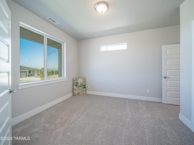 carpeted spare room with a wealth of natural light, visible vents, and baseboards