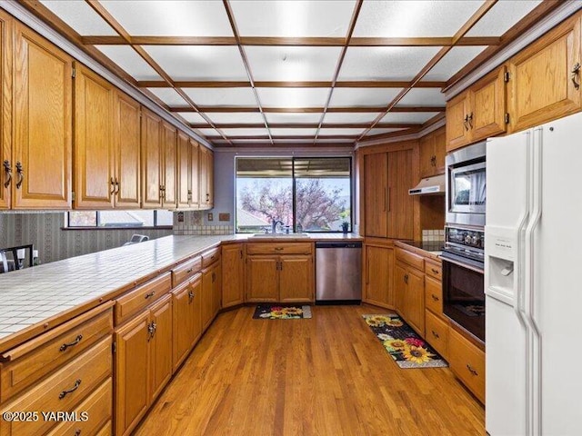 kitchen featuring brown cabinetry, light wood-style floors, tile counters, black appliances, and a sink