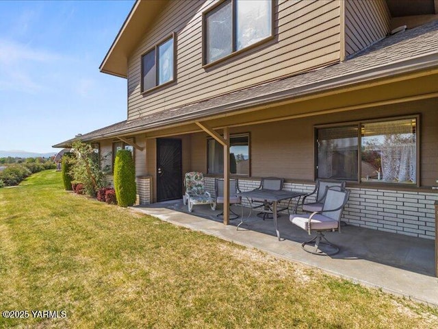 back of property with a patio, a yard, and roof with shingles