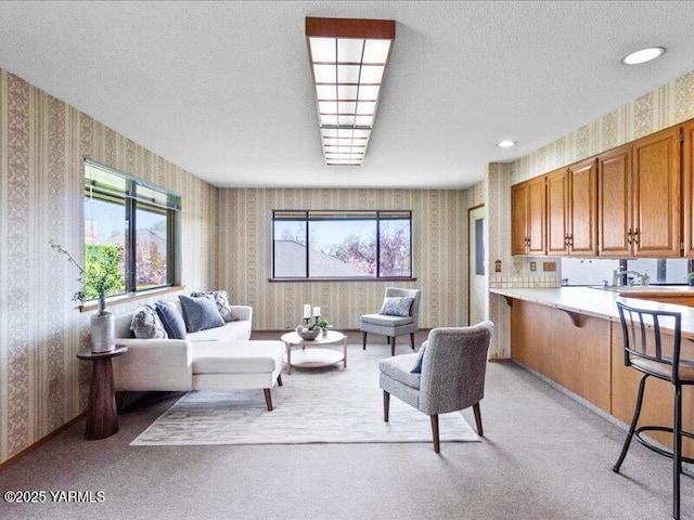 living room with a textured ceiling, wallpapered walls, and light colored carpet