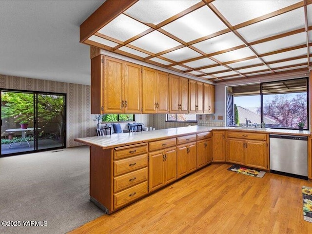 kitchen featuring stainless steel dishwasher, a sink, tile counters, wallpapered walls, and a peninsula