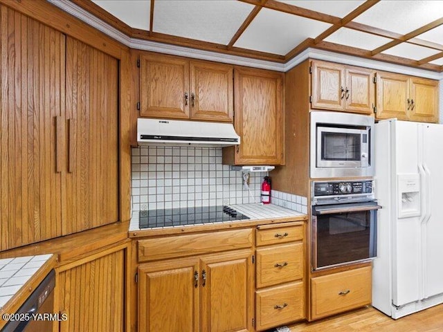 kitchen with black appliances, tile counters, tasteful backsplash, and range hood