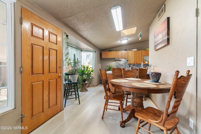 dining space with lofted ceiling with skylight, light wood-type flooring, a textured ceiling, and visible vents