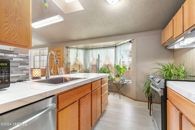 kitchen featuring light wood-type flooring, a textured ceiling, a sink, backsplash, and stainless steel appliances