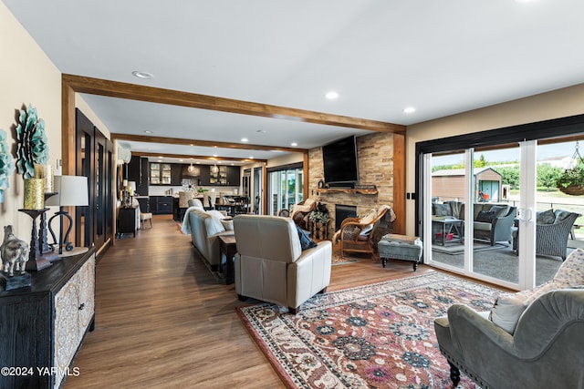 living area with recessed lighting, beam ceiling, a stone fireplace, and wood finished floors