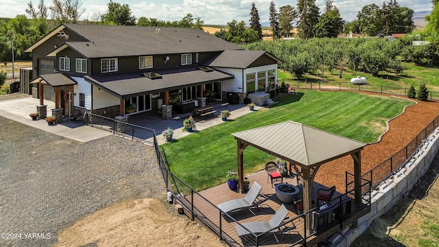 back of property with fence, dirt driveway, a gazebo, stone siding, and board and batten siding