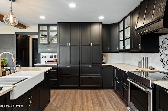 kitchen with glass insert cabinets, stainless steel range with electric cooktop, light countertops, light wood-type flooring, and decorative light fixtures