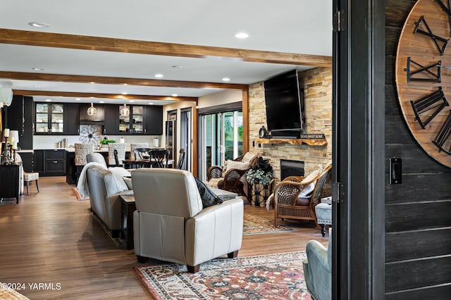 living area featuring recessed lighting, beam ceiling, a stone fireplace, and wood finished floors