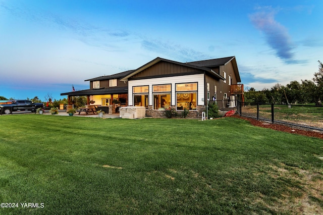 back of house at dusk with a yard, board and batten siding, a patio area, and fence