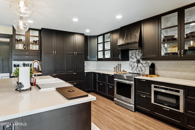 kitchen featuring custom range hood, glass insert cabinets, hanging light fixtures, light countertops, and stainless steel range with electric stovetop