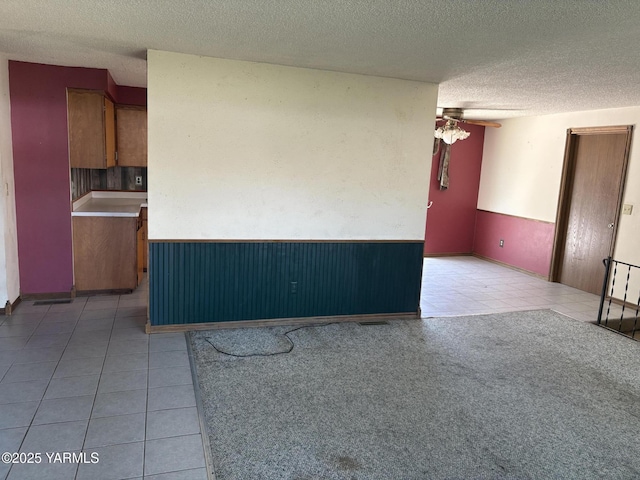 unfurnished living room featuring ceiling fan, a textured ceiling, a wainscoted wall, and light tile patterned floors