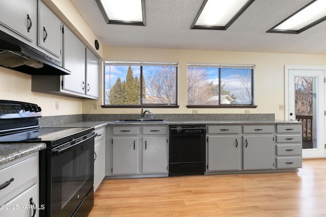 kitchen featuring black appliances, a sink, light wood-style flooring, and under cabinet range hood