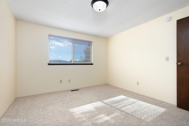 carpeted spare room with visible vents and a textured ceiling