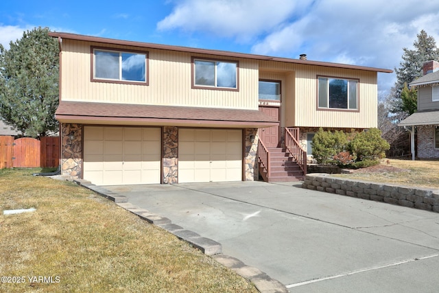 split foyer home with concrete driveway, fence, a garage, stone siding, and a front lawn