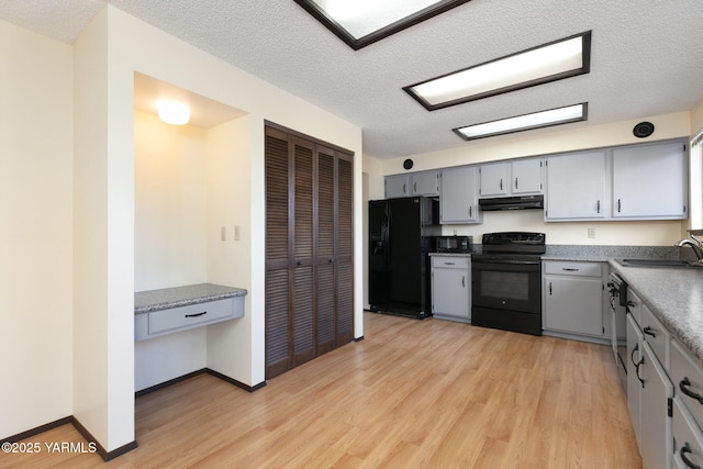 kitchen featuring black appliances, a sink, light wood-style flooring, and under cabinet range hood