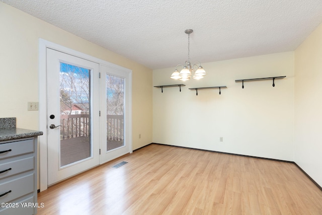 unfurnished dining area featuring a textured ceiling, an inviting chandelier, visible vents, and light wood-style floors