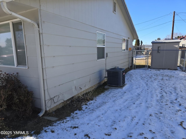 snow covered property featuring cooling unit, a gate, and fence